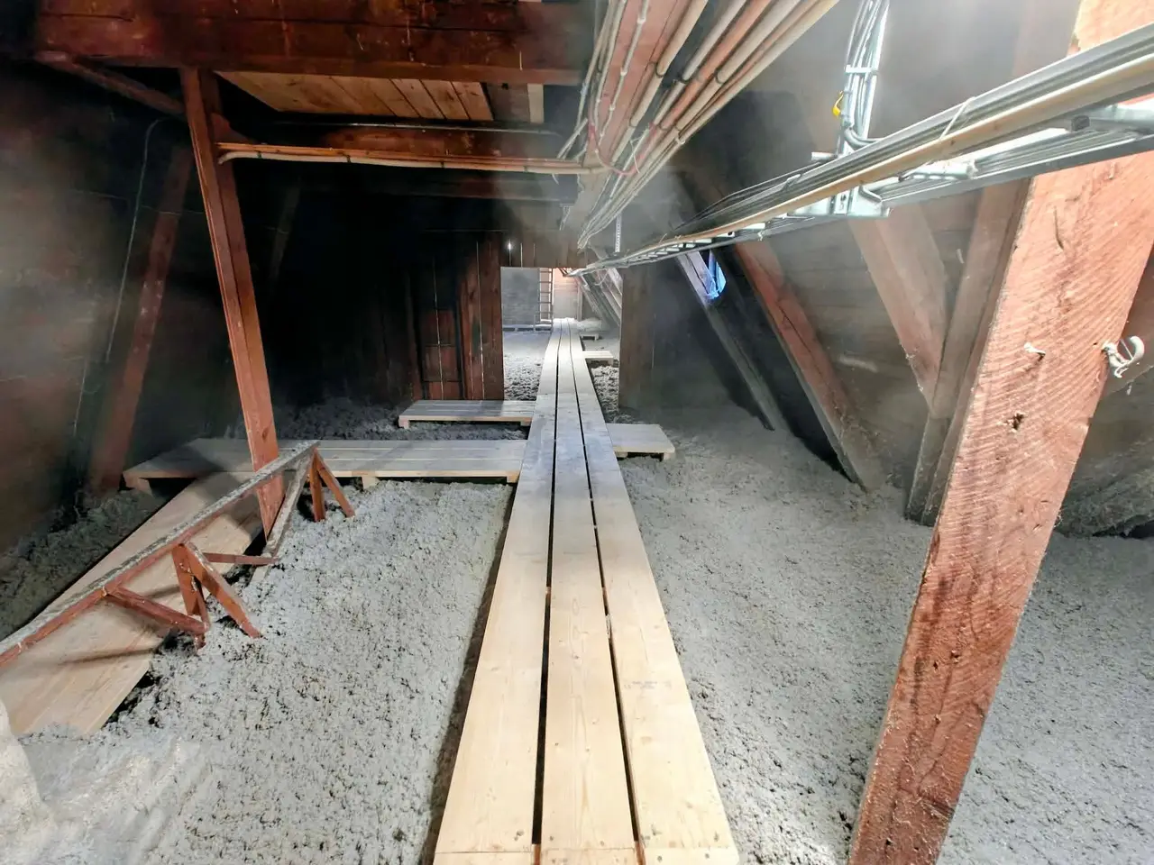 Lång vind i flerbostadshus med lösull och gångplankor